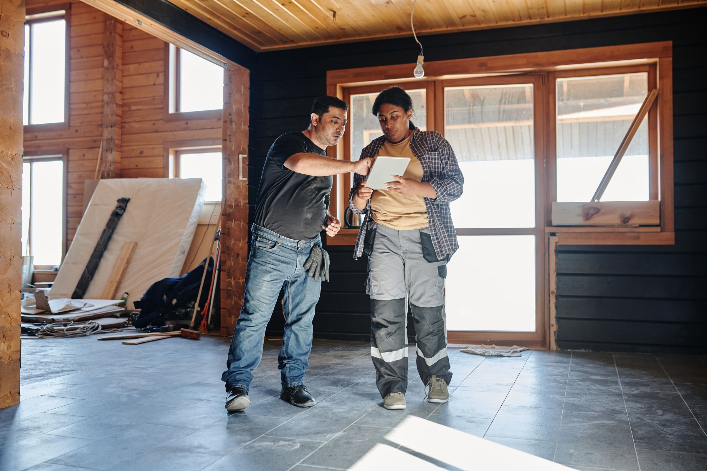 A builder points across a timber-lined room under fit-out while a colleague checks the job on a tablet
